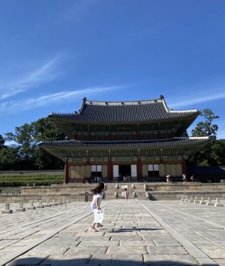 A child running across the stone courtyard in front of Injeongjeon Hall beneath a deep blue summer sky
