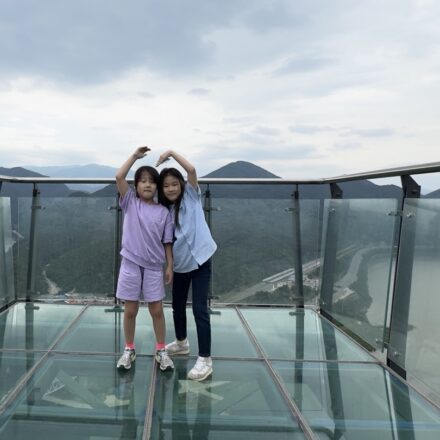 Two sisters standing together and making heart shapes above their heads on the glass skywalk