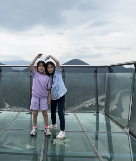Two sisters standing together and making heart shapes above their heads on the glass skywalk