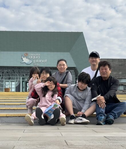 Our seven-person family posing on the steps outside Aqua Planet Jeju