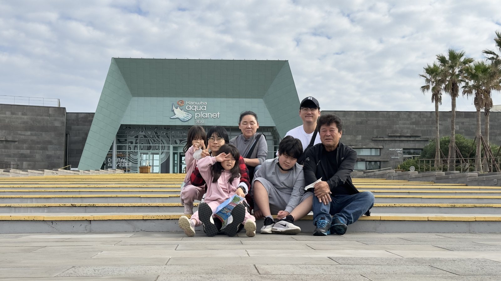 아쿠아플라넷 제주 입구 계단에서 기념사진을 찍는 일곱 명의 가족